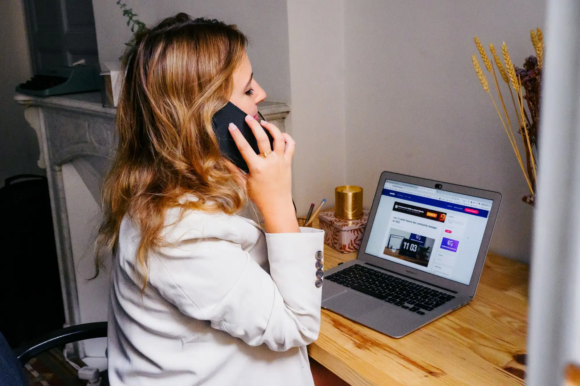 Woman at a wooden desk on a phone call with a laptop open in front of her