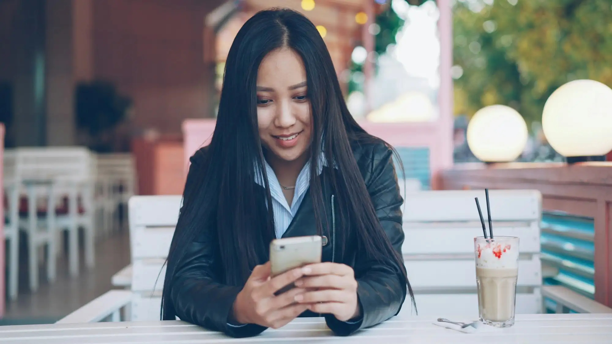 Young woman smiling as she reads a message on her phone at a café table