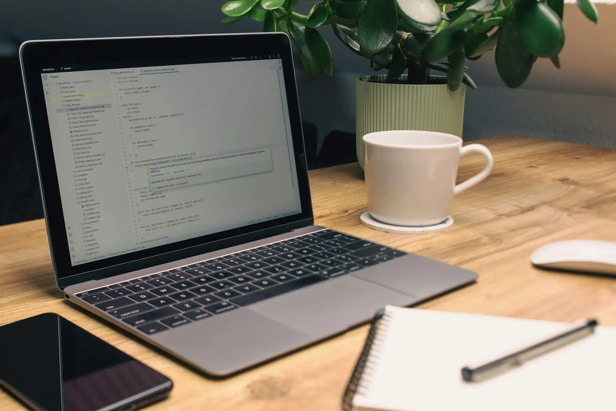Laptop, notebook, phone and a mug on a tidy wooden desk