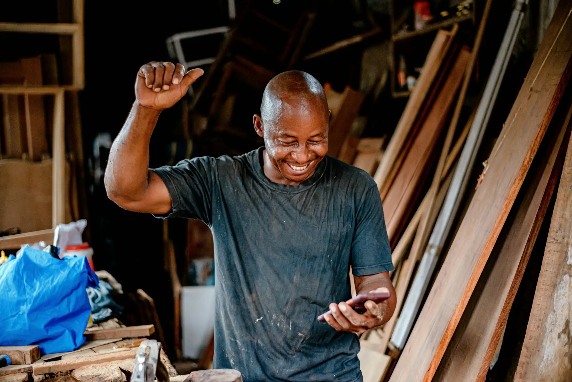 Workshop owner smiling and raising his fist as he reads good news on his phone